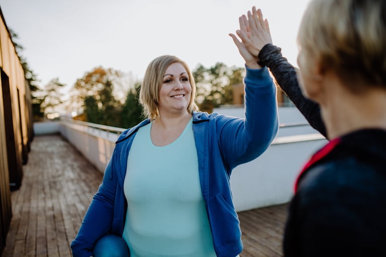 A happy overweight woman high fiving with personal trainer outdoors on gym terrace