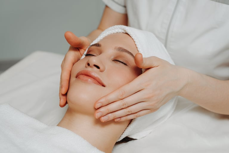 face massage, young attractive caucasian woman, beautiful relaxed lady with closed eyes smiling, white towel, spa therapist doing facial and head massage in beauty salon