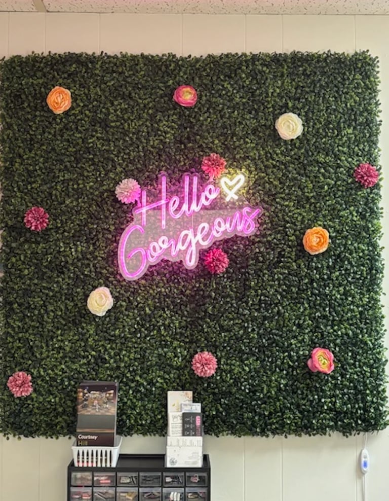 Neon Hello Gorgeous sign on artificial green moss wall with decorative pink and orange flowers