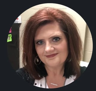 Portrait of a woman with shoulder-length reddish-brown hair, hoop earrings, and a subtle smile against a dark background