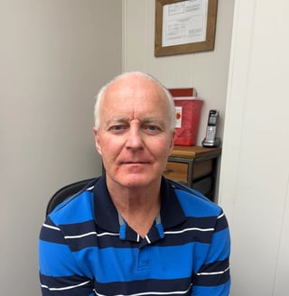 Older man with white hair wearing a blue and navy striped polo shirt, photographed indoors