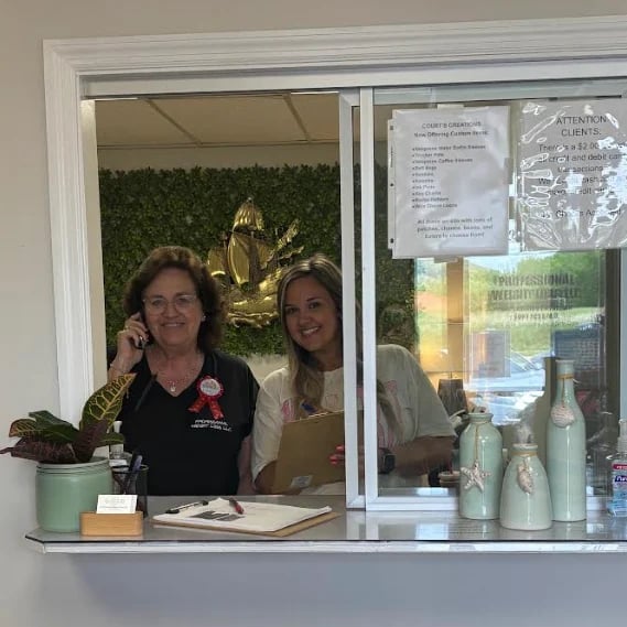 Two women working at a service counter with a green wall backdrop and golden decorative sculpture behind them