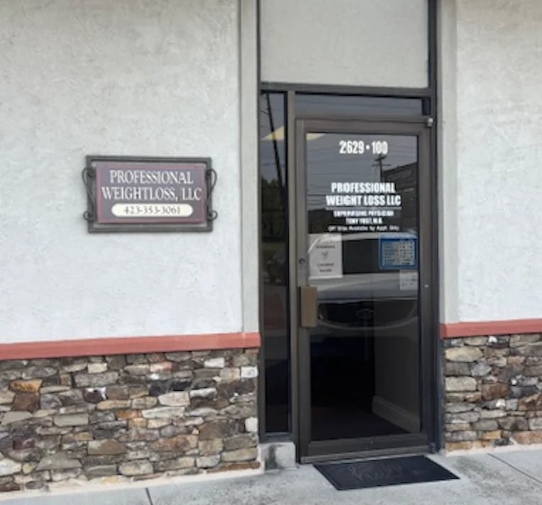 Storefront entrance for Professional Weightloss LLC with brown sign and black glass door on stone-trimmed white wall