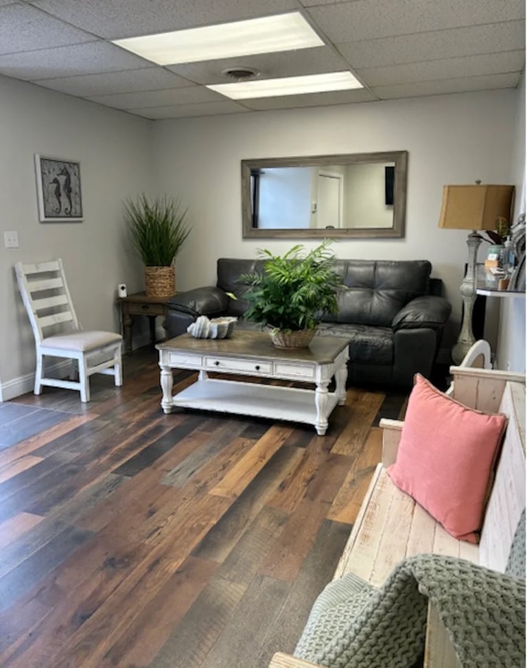 Modern office waiting room with black leather sofa, white coffee table, wooden floors, plants, and comfortable seating arrangements